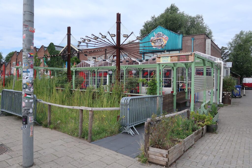 Terras van horecagelegenheid Pizza Territory aan het Gedempt Hamerkanaal in Amsterdam, omgeven door planten en decoratieve verlichting.